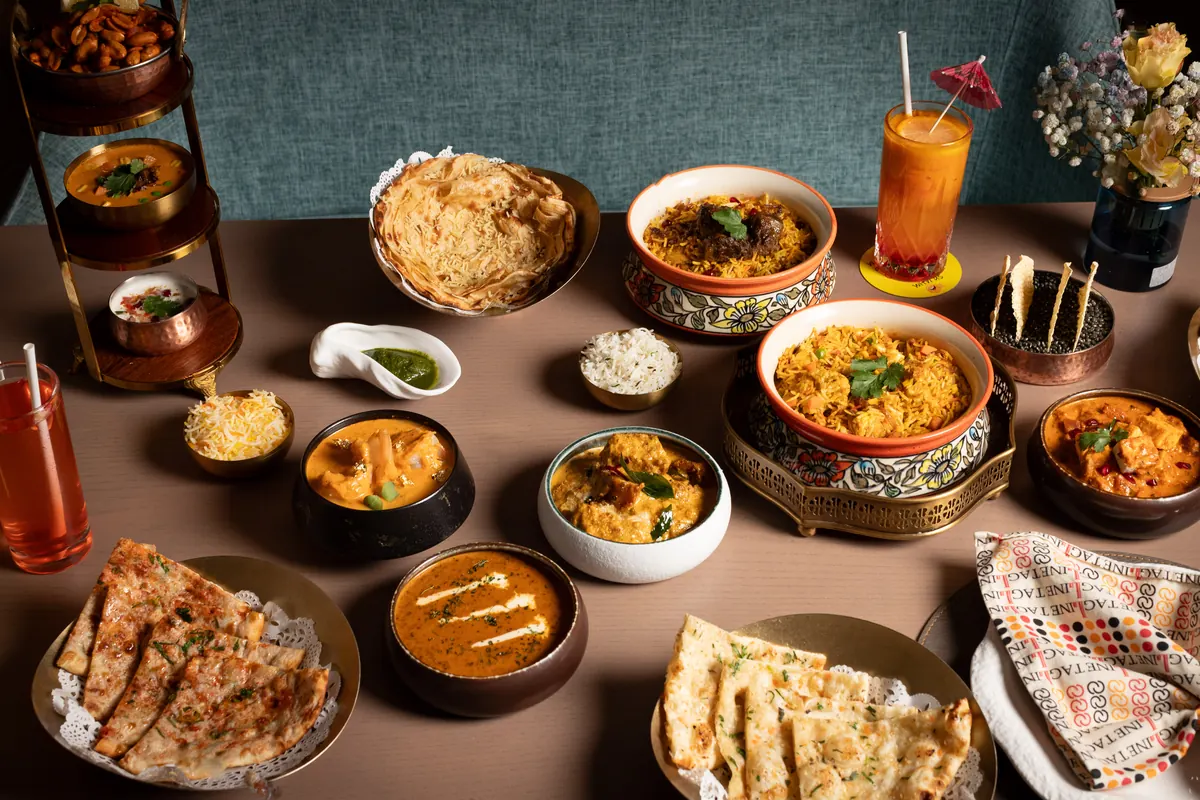 A table full of curries, biryani, breads and drinks beside Tagline’s teal banquette