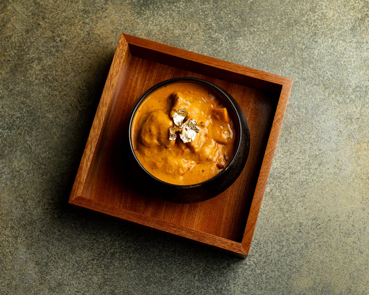 24K Gold Butter Chicken from above: a black bowl topped with gold leaf, in a wooden box