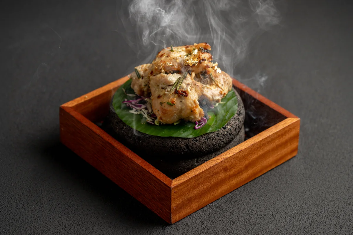 24K chicken malai tikka on a smoking stone in a wooden box