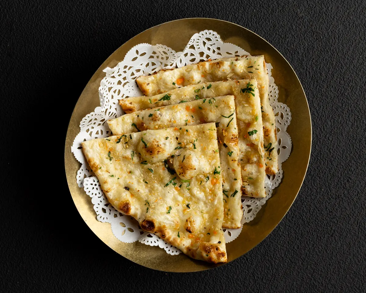 Garlic naan, cut into wedges and scattered with coriander, on a brass plate