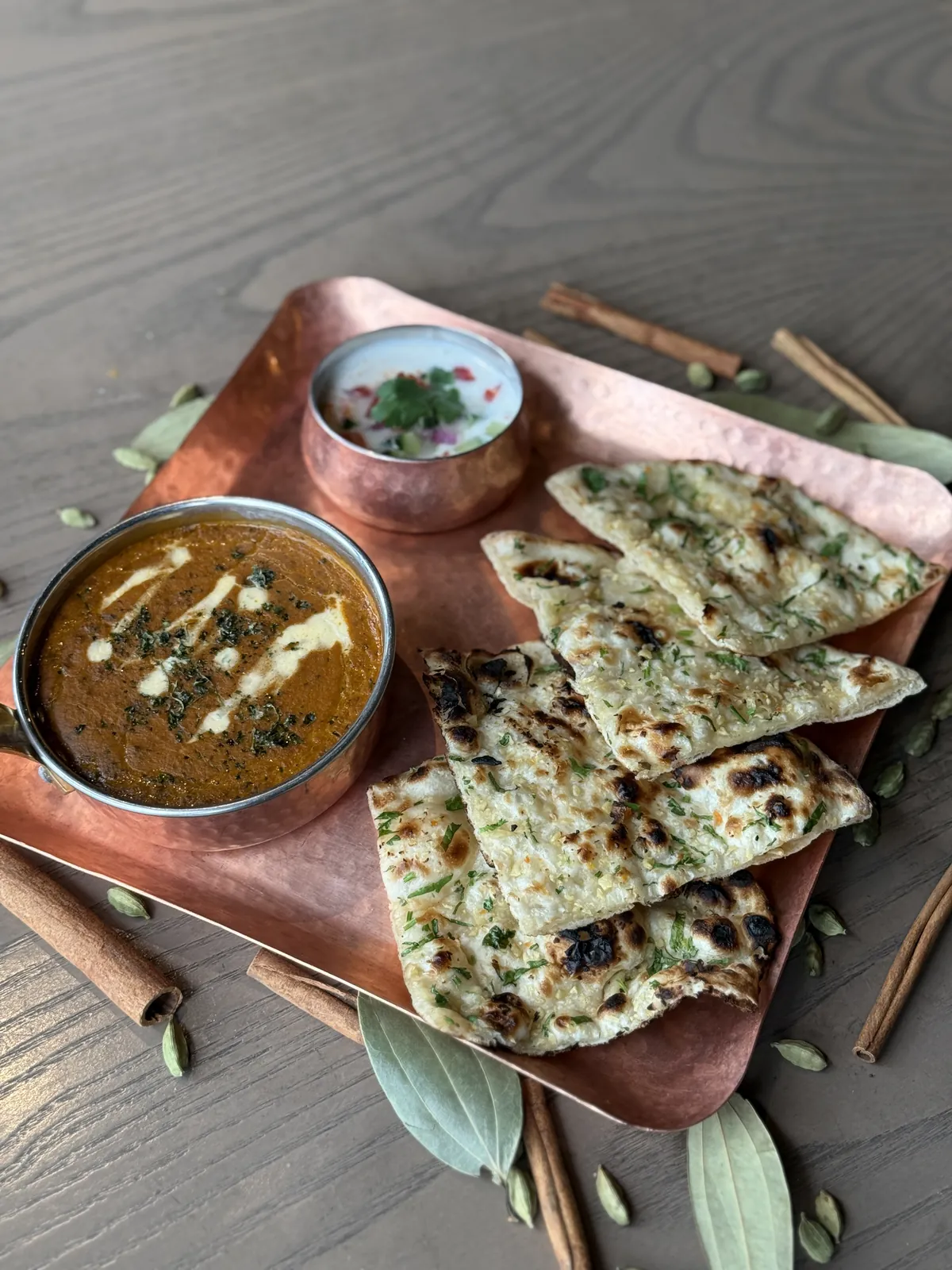 A mini set lunch on a copper tray: a curry, naan and raita