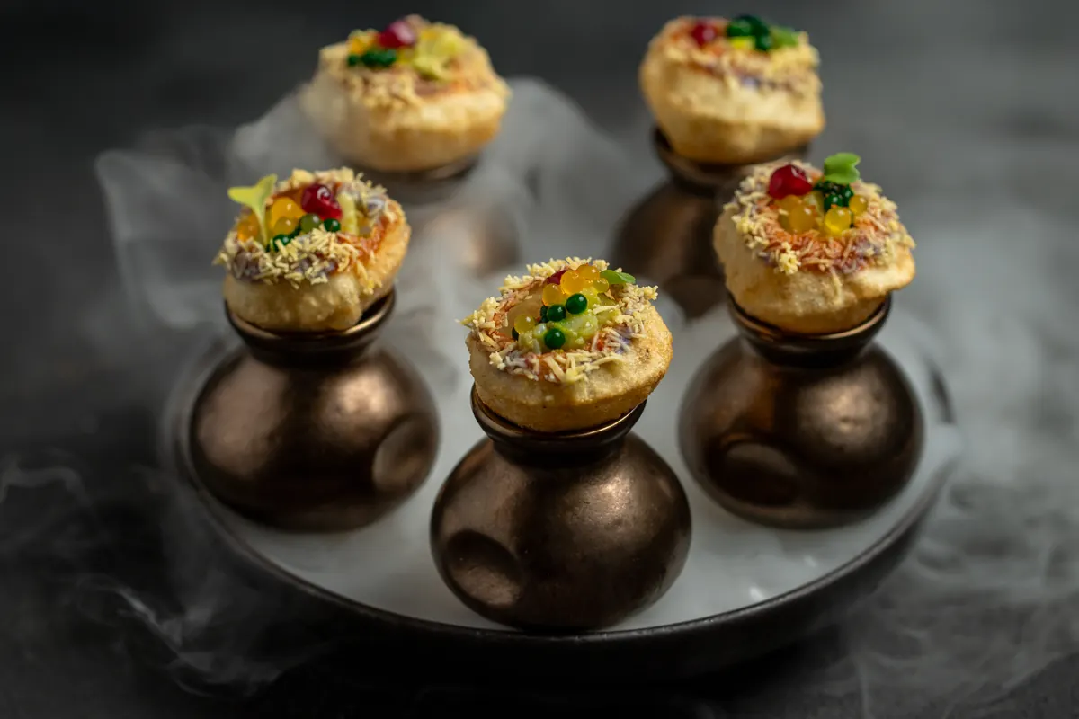 Pani puri sitting on small bronze clay pots in a drift of mist