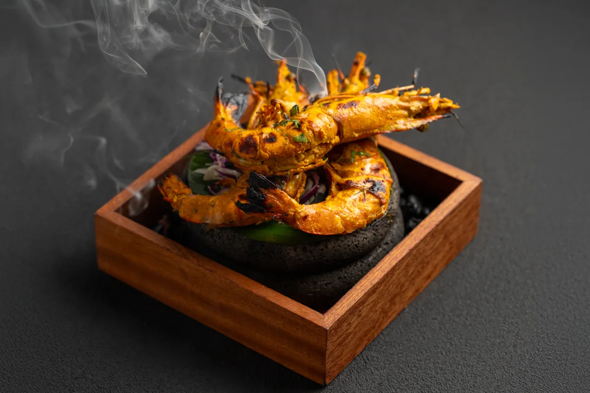 Kesri tandoori prawns piled on a stone in a wooden box