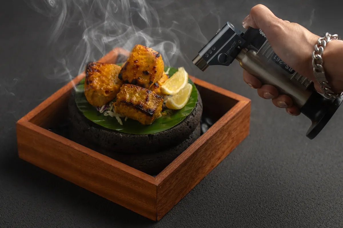 Salmon tikka on a smoking stone in a wooden box, finished with a kitchen blowtorch